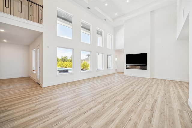 unfurnished living room featuring recessed lighting, light wood-type flooring, baseboards, and a towering ceiling