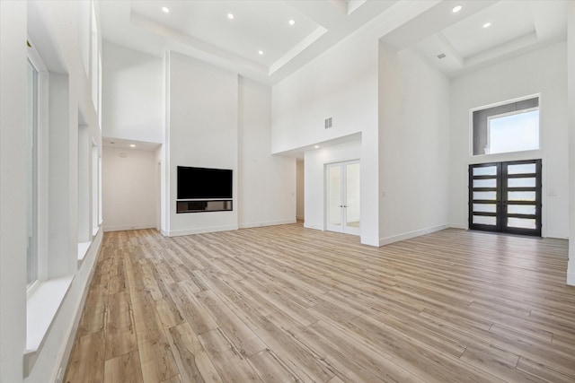 unfurnished living room featuring a towering ceiling, light hardwood / wood-style floors, and french doors