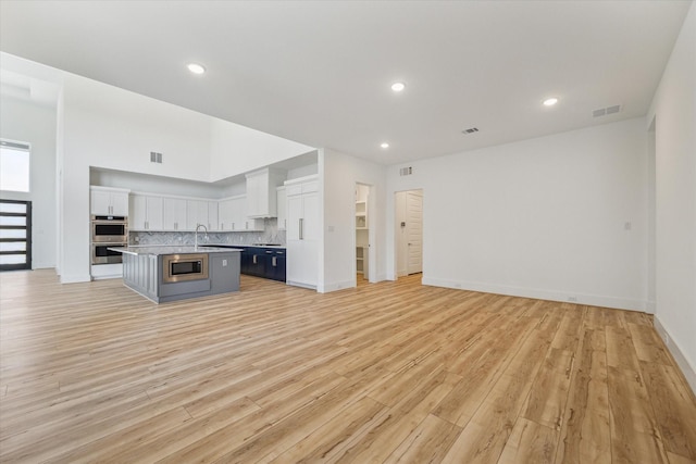 kitchen featuring an island with sink, tasteful backsplash, open floor plan, white cabinetry, and stainless steel appliances