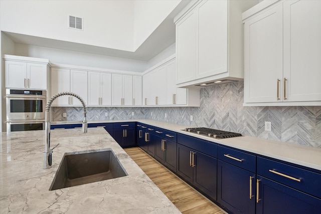 kitchen with blue cabinetry, sink, light stone counters, appliances with stainless steel finishes, and white cabinets