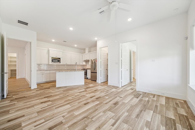 kitchen with white cabinetry, decorative backsplash, light hardwood / wood-style floors, stainless steel appliances, and a center island with sink