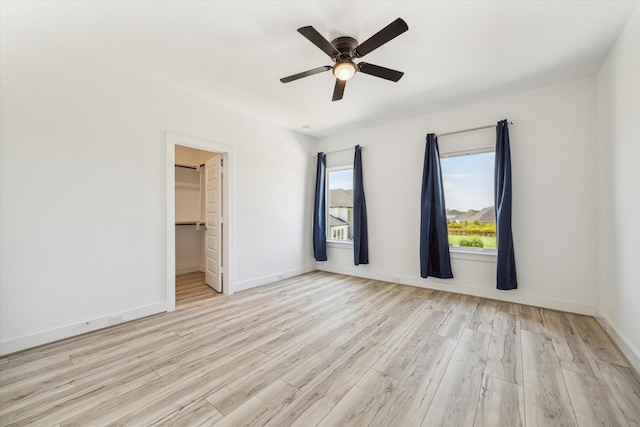 unfurnished bedroom featuring ceiling fan, a walk in closet, baseboards, and wood finished floors