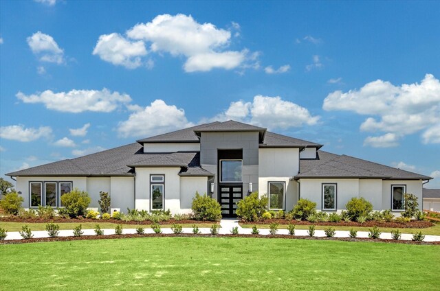 view of front facade with stucco siding, a front yard, and a shingled roof