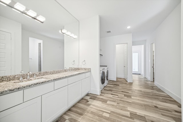 bathroom with visible vents, double vanity, separate washer and dryer, wood finished floors, and a sink