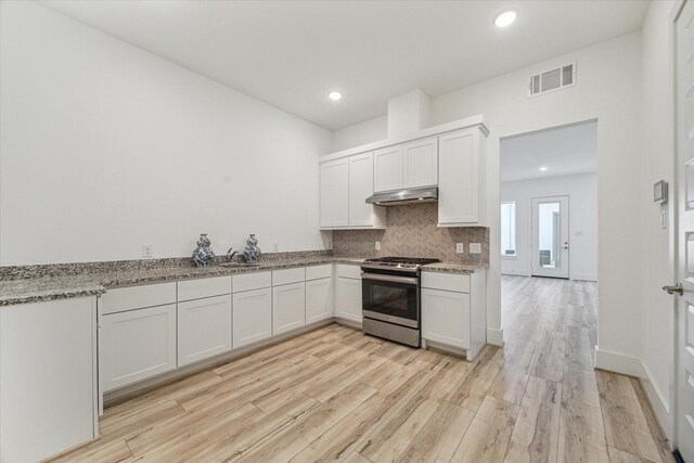 kitchen featuring light stone counters, backsplash, stainless steel gas range oven, and white cabinets