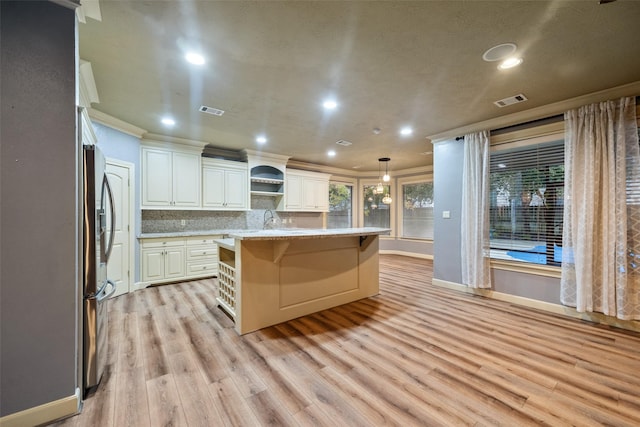 kitchen with pendant lighting, ornamental molding, an island with sink, and white cabinets