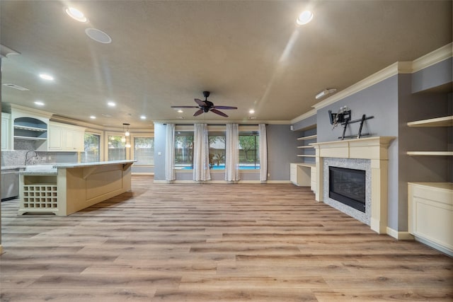 unfurnished living room featuring sink, light wood-type flooring, ornamental molding, a tile fireplace, and ceiling fan