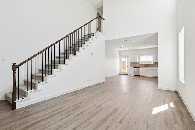 unfurnished living room featuring a high ceiling, sink, and light hardwood / wood-style floors