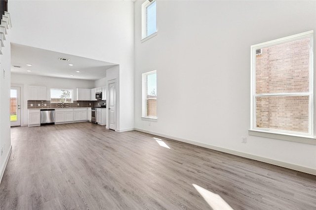 unfurnished living room with sink, a towering ceiling, and light wood-type flooring