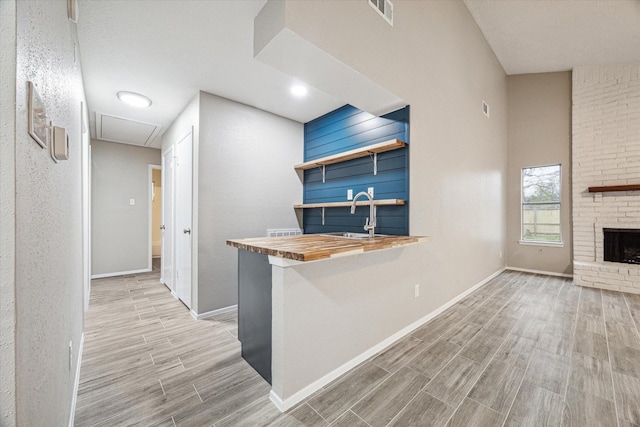 kitchen featuring sink, a breakfast bar area, wooden counters, kitchen peninsula, and a fireplace