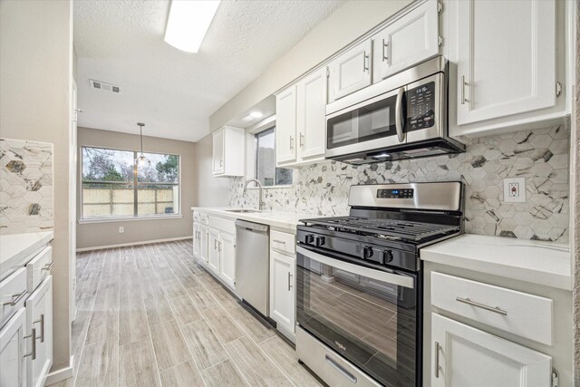 kitchen featuring sink, white cabinets, hanging light fixtures, stainless steel appliances, and light stone countertops