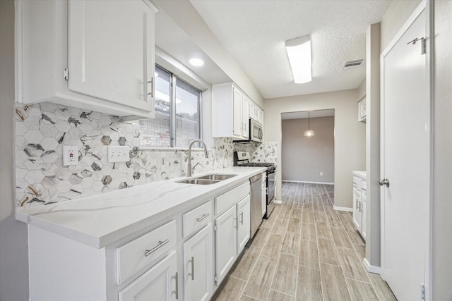 kitchen with white cabinetry, sink, backsplash, light stone counters, and stainless steel appliances