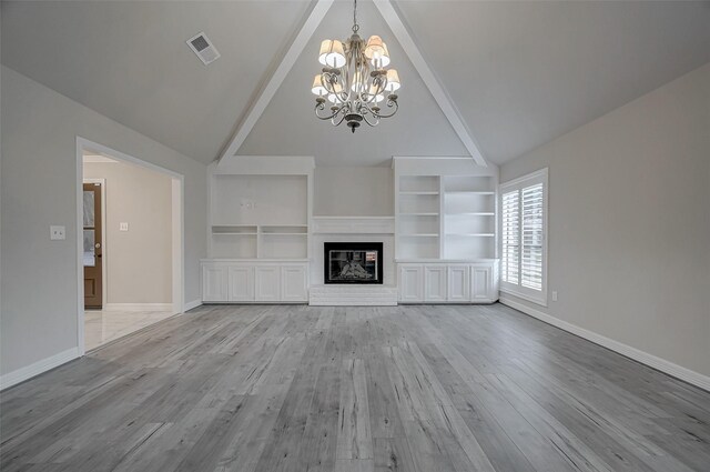 unfurnished living room with lofted ceiling with beams, a notable chandelier, a fireplace, and light hardwood / wood-style floors