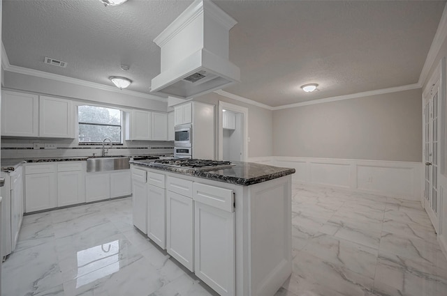 kitchen with sink, premium range hood, white cabinetry, stainless steel appliances, and a center island