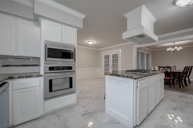 kitchen featuring white cabinetry, appliances with stainless steel finishes, custom range hood, and crown molding