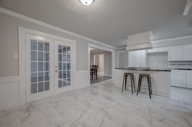 kitchen with crown molding, a breakfast bar, white cabinetry, a textured ceiling, and french doors