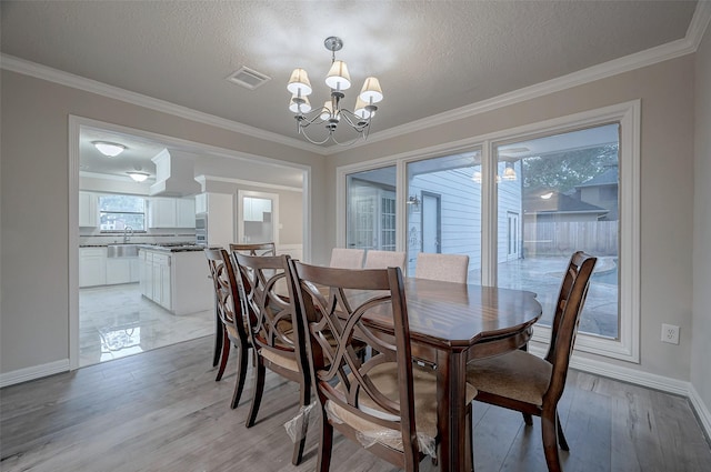 dining space with a textured ceiling, ornamental molding, light hardwood / wood-style floors, and a chandelier