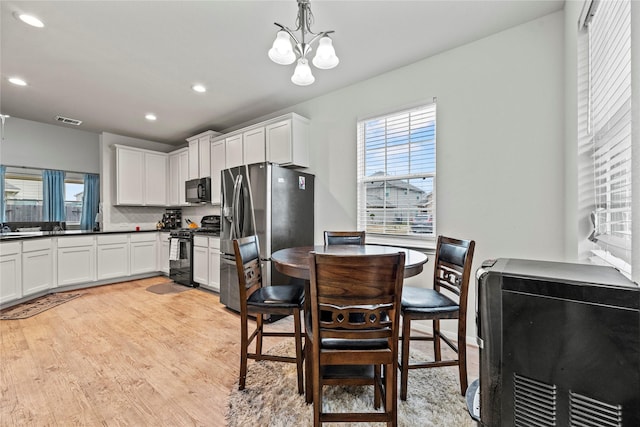 kitchen featuring white cabinetry, tasteful backsplash, black appliances, decorative light fixtures, and light wood-type flooring