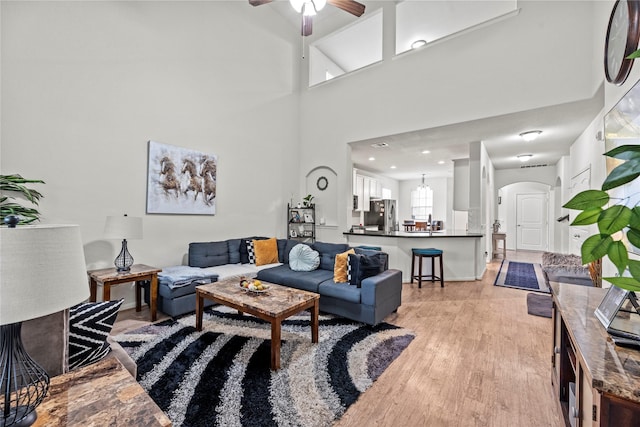 living room featuring a towering ceiling, light hardwood / wood-style floors, and ceiling fan