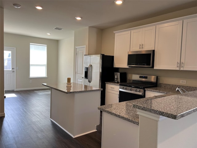 kitchen featuring dark hardwood / wood-style floors, white cabinetry, a center island, stainless steel appliances, and light stone countertops