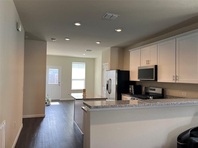 kitchen with dark hardwood / wood-style floors, white cabinets, kitchen peninsula, stainless steel appliances, and light stone countertops