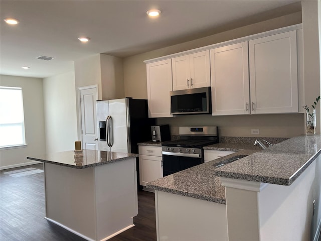 kitchen with dark stone countertops, stainless steel appliances, a kitchen island, and white cabinets