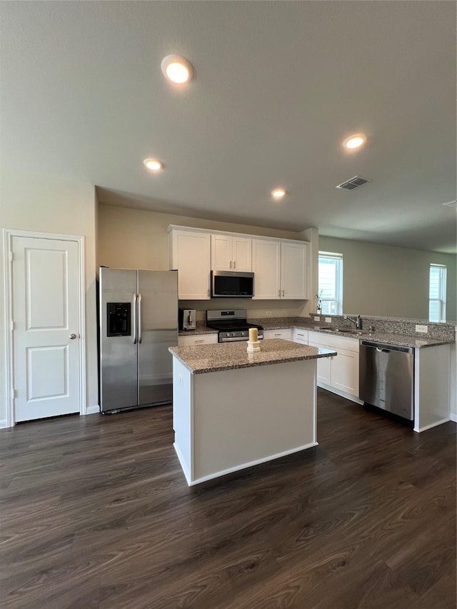 kitchen featuring dark wood-type flooring, stainless steel appliances, white cabinets, and a kitchen island