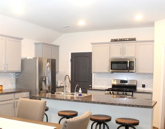 kitchen with dark stone counters, appliances with stainless steel finishes, a sink, and a kitchen breakfast bar