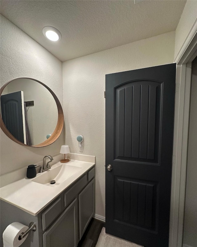 bathroom with a textured ceiling, a textured wall, wood finished floors, and vanity