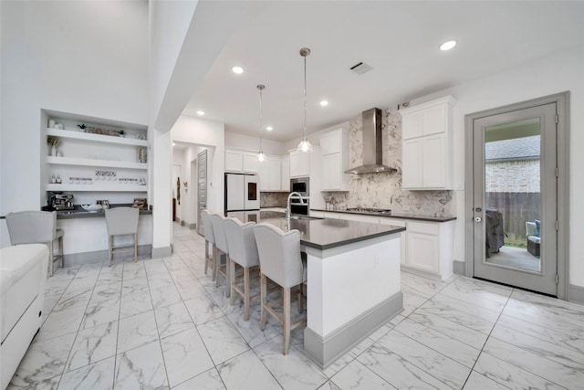 kitchen featuring pendant lighting, white cabinets, a kitchen bar, and wall chimney exhaust hood