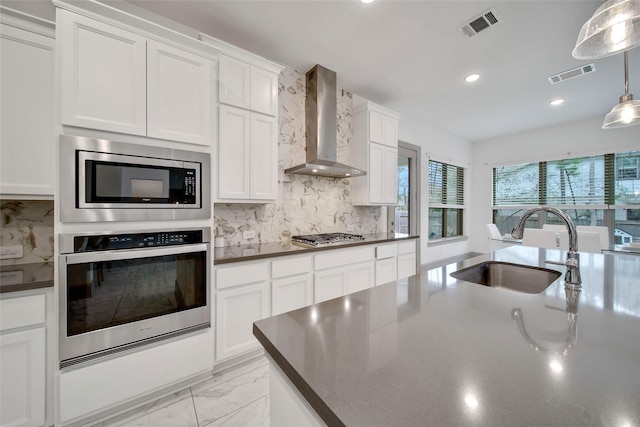 kitchen with wall chimney exhaust hood, sink, white cabinetry, appliances with stainless steel finishes, and pendant lighting