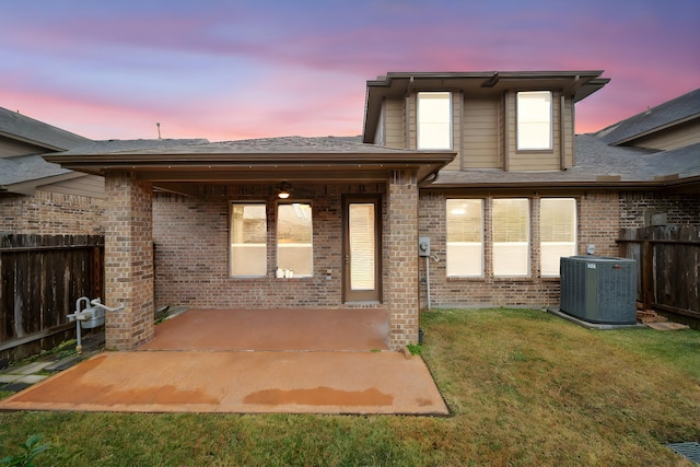 back house at dusk featuring a patio, central AC, and a lawn