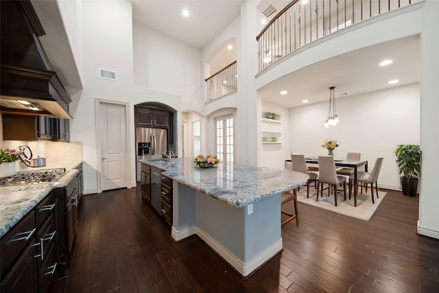 kitchen with a breakfast bar area, a kitchen island with sink, dark hardwood / wood-style flooring, custom exhaust hood, and stainless steel gas stovetop