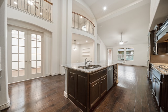 kitchen featuring french doors, dark brown cabinetry, sink, stainless steel dishwasher, and an island with sink