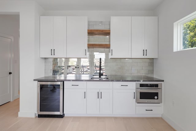 kitchen featuring white cabinets, stainless steel oven, beverage cooler, and backsplash