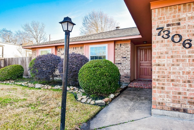 view of exterior entry with fence and brick siding