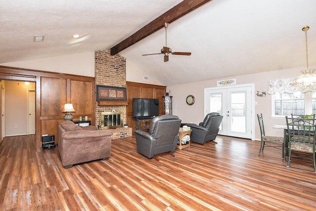 living area with french doors, beamed ceiling, a brick fireplace, and light wood-style flooring