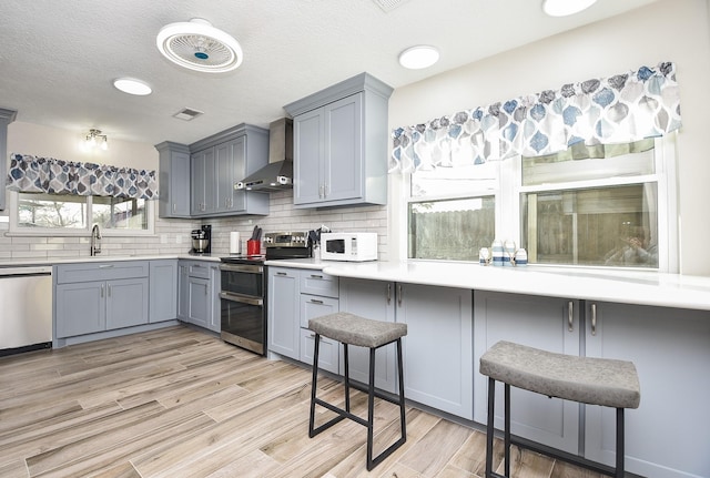 kitchen with wall chimney exhaust hood, gray cabinets, white microwave, double oven range, and dishwashing machine