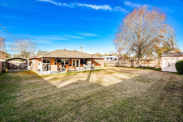 rear view of house featuring a lawn, a patio, a fenced backyard, an outdoor structure, and a detached carport