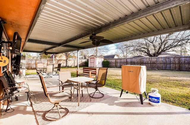 view of patio with outdoor dining area, ceiling fan, a shed, a fenced backyard, and an outdoor structure