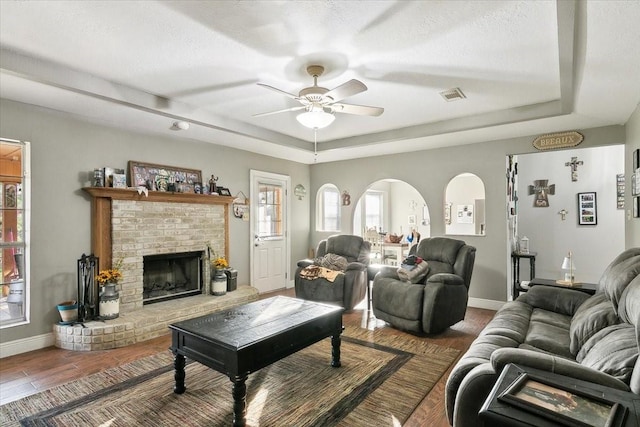 living room featuring hardwood / wood-style flooring, ceiling fan, a fireplace, and a raised ceiling