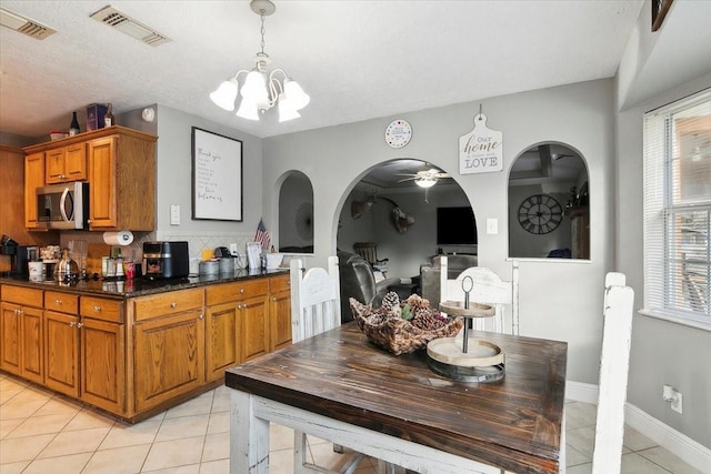 kitchen featuring a textured ceiling, hanging light fixtures, light tile patterned floors, dark stone counters, and decorative backsplash