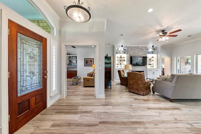 foyer with crown molding, ceiling fan, light wood-type flooring, and a fireplace