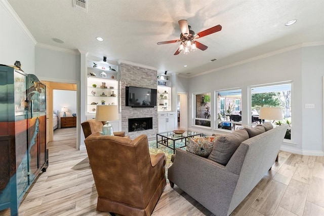 living room featuring ornamental molding, a large fireplace, ceiling fan, and light wood-type flooring