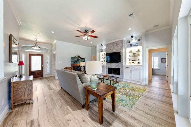 living room featuring crown molding, ceiling fan, a fireplace, and light wood-type flooring