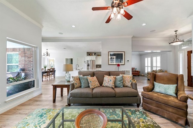 living room featuring crown molding, ceiling fan with notable chandelier, sink, and light hardwood / wood-style flooring