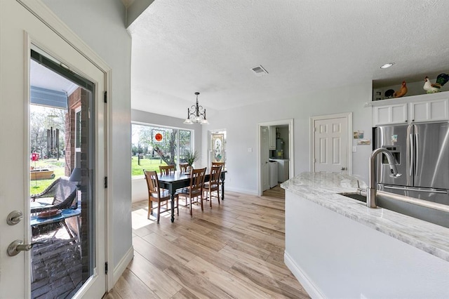 kitchen with light stone countertops, light hardwood / wood-style floors, white cabinets, a textured ceiling, and decorative light fixtures