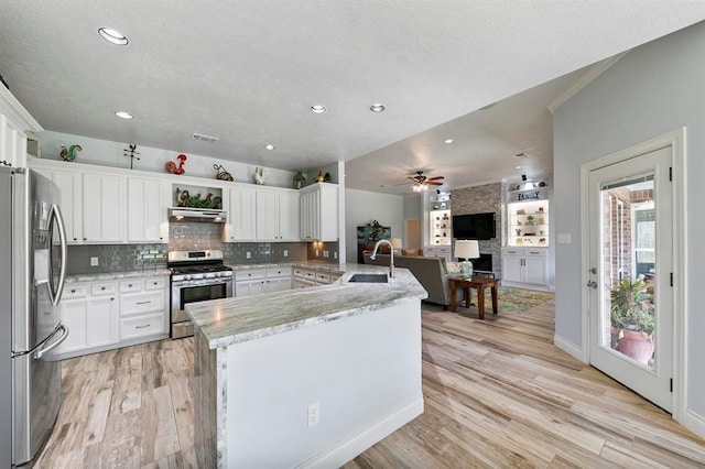 kitchen with white cabinetry, appliances with stainless steel finishes, light stone counters, and kitchen peninsula