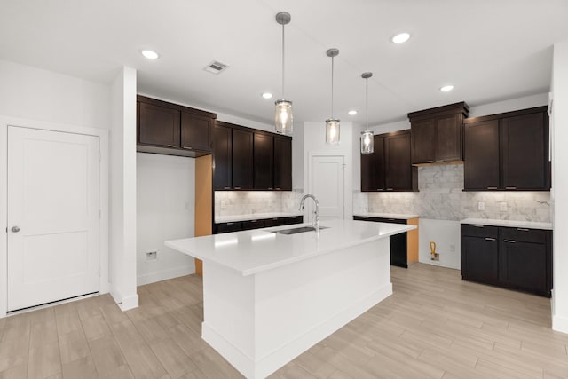 kitchen with hanging light fixtures, sink, a center island with sink, and dark brown cabinetry