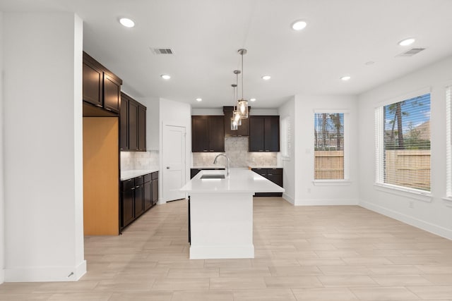 kitchen featuring pendant lighting, sink, backsplash, a kitchen island with sink, and dark brown cabinets